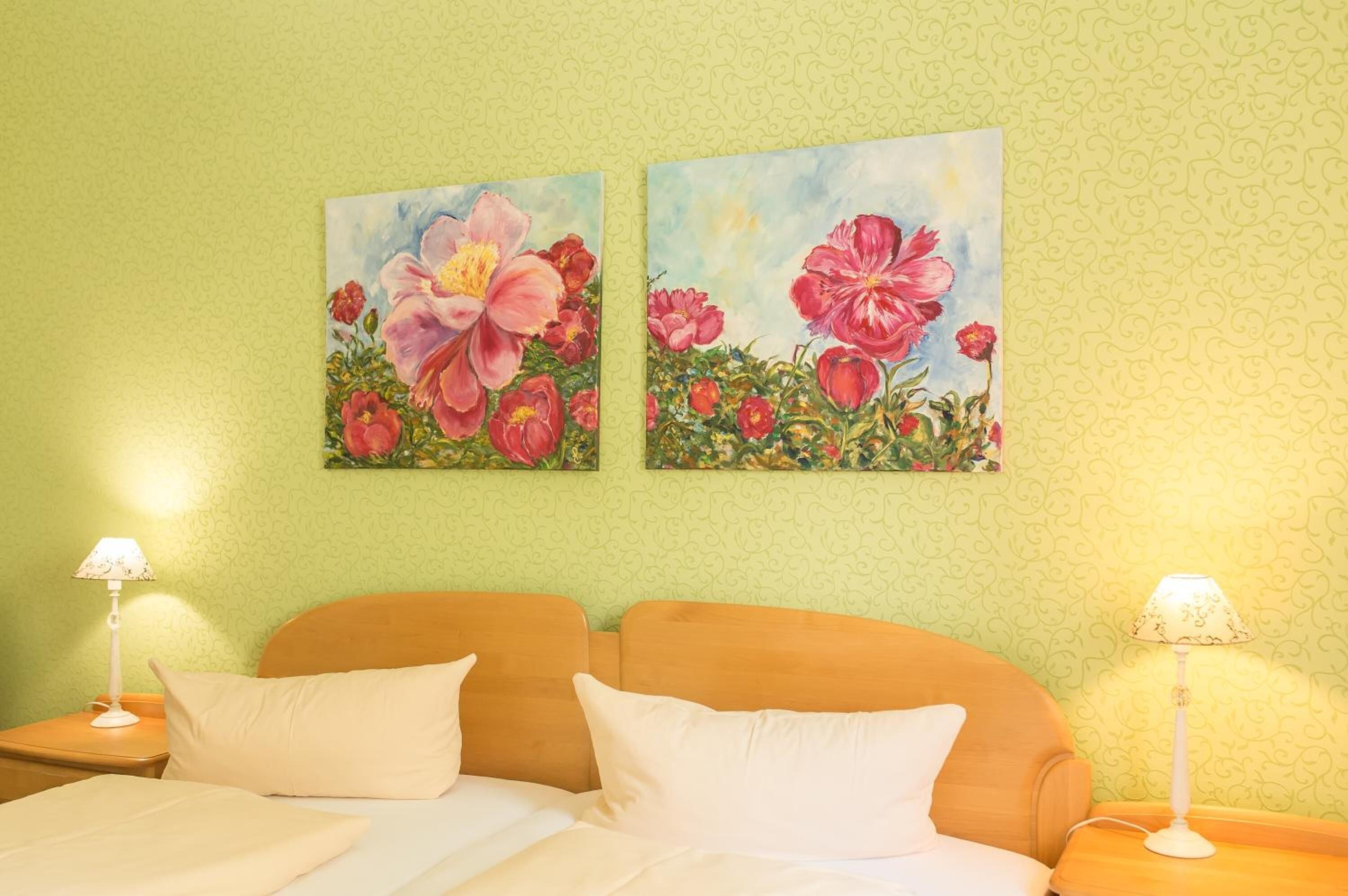 A hotel room with a bed, two nightstands, two lamps, and two floral paintings on the wall.