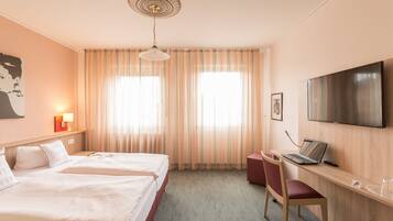 A hotel room with two beds, a desk with a laptop, a TV, and a large window with curtains.