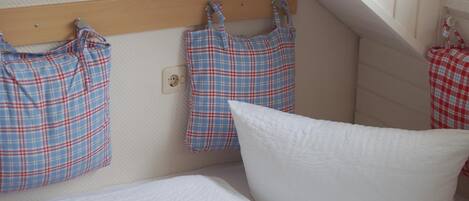 A bedroom with a bed, a white pillow, and plaid-patterned bags hanging on a wooden shelf.