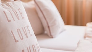 Una habitación de hotel con una cama, un almohadón con la inscripción "LIVE LOVE LAUGH" y una lámpara fijada a la pared.