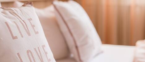 A hotel room with a bed, a pillow with the text "LIVE LOVE LAUGH," and a wall-mounted lamp.