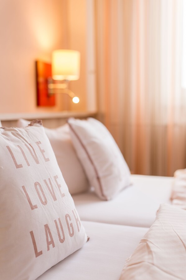 A hotel room with a bed, a pillow with the text "LIVE LOVE LAUGH," and a wall-mounted lamp. - Hotel Restaurant Leander (Bitburg)