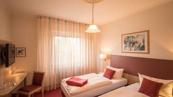 A hotel room with a bed, a chair, a desk, and a painting on the wall.