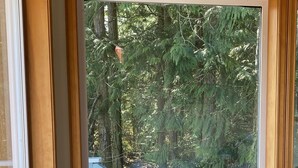 Un escritorio de madera con un libro y un florero, situado cerca de un ventanal con vistas a una zona boscosa.