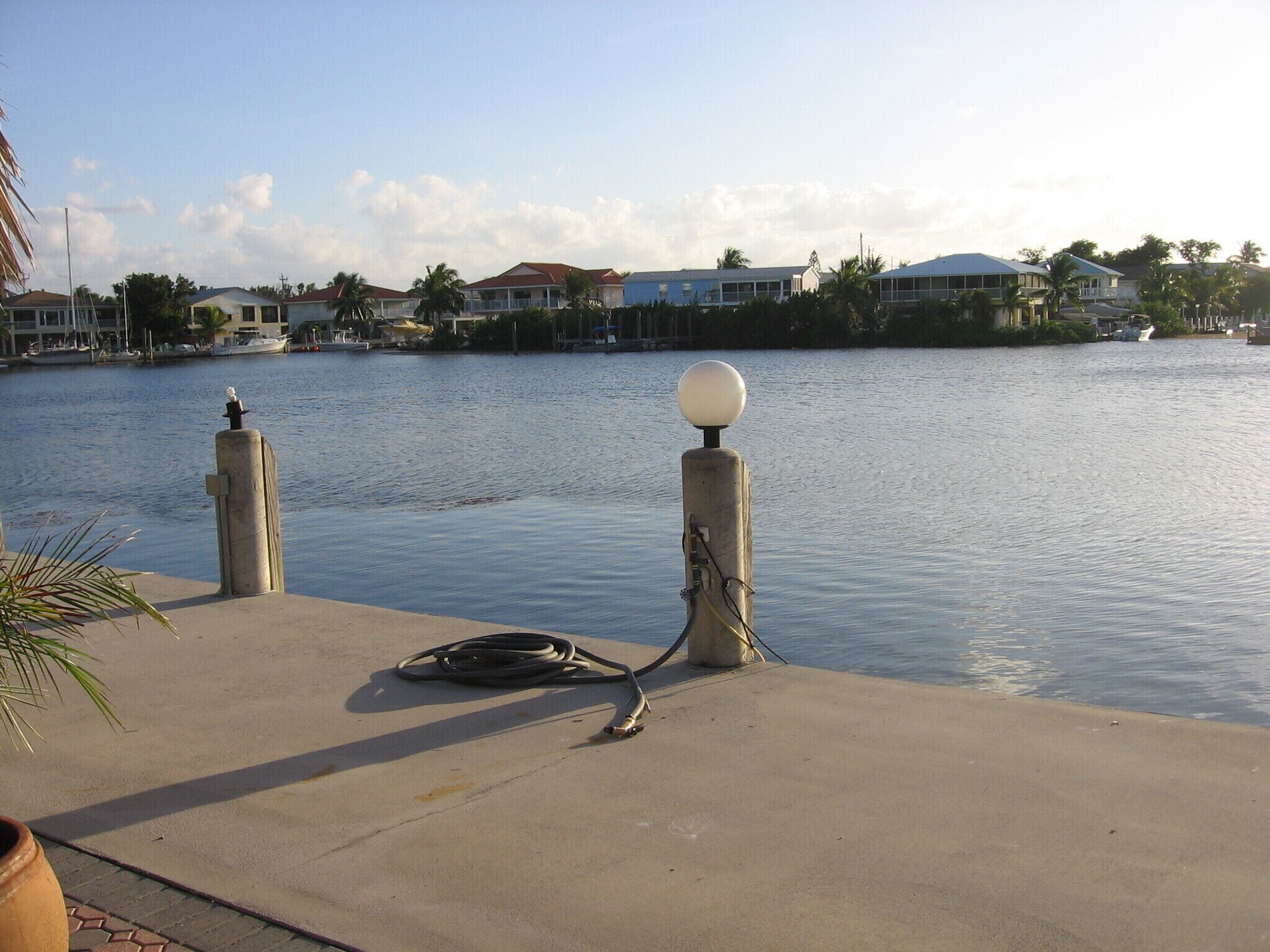A waterfront view with a concrete dock, a lamp post, and a hose on the ground.