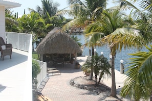 A thatched-roof structure with outdoor seating, a paved pathway, and palm trees.