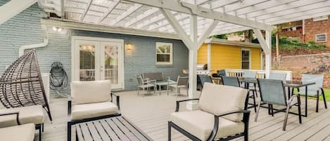 An outdoor patio with a covered seating area, a grill, and a blue building in the background.
