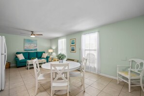 A living room with a teal sofa, white chairs, a round table, and a ceiling fan.