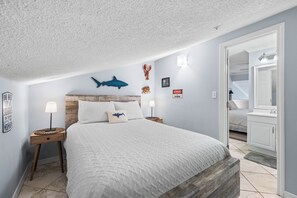 Camera da letto con un letto, una testiera in legno, decorazioni a parete e lampade ai lati del letto, con vista sul bagno.