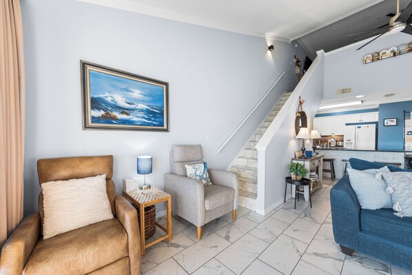 A living room with a sofa, armchair, and a chair, a staircase, and a kitchen area.