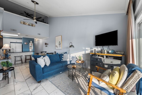 Un soggiorno moderno con un divano blu, un tavolino da caffè, una TV e un'area pranzo con una cucina sullo sfondo.