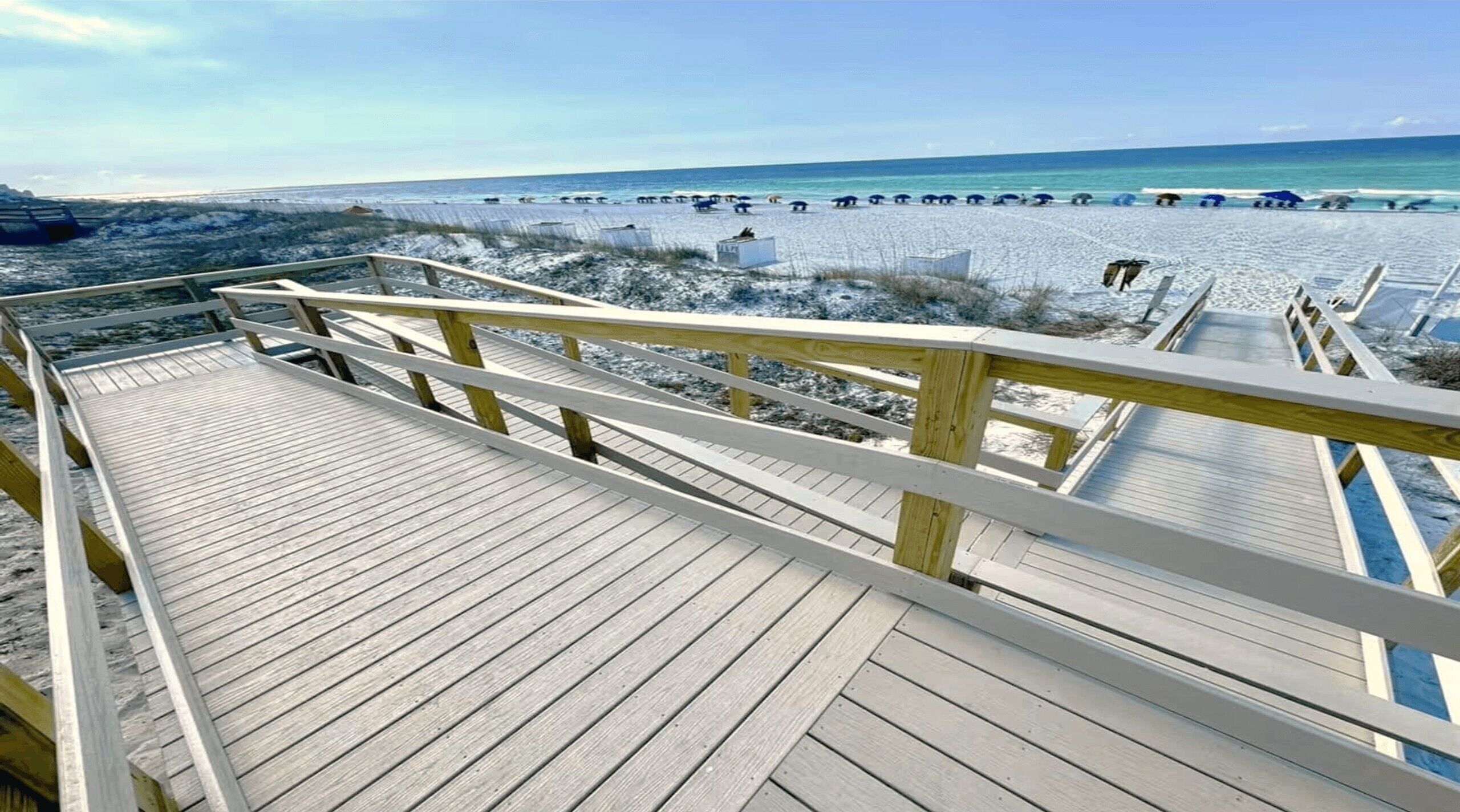 Ein Holzsteg führt zu einem Strand bei blauem Himmel.