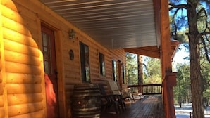 Een houten hut met een overdekte veranda, een vat en een bank.