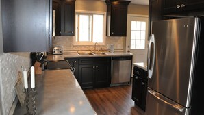 A modern kitchen with dark cabinetry, stainless steel appliances, and a central island. - 4 Bedroom, 2 Bath  Wooded Getaway (Boyne Falls)