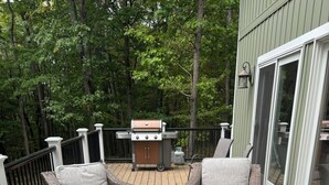 A deck with wicker chairs, a grill, and a table with a mug. - 4 Bedroom, 2 Bath  Wooded Getaway (Boyne Falls)