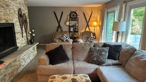 A cozy living room with a stone fireplace, a sectional sofa, and decorative skis on the wall. - 4 Bedroom, 2 Bath  Wooded Getaway (Boyne Falls)
