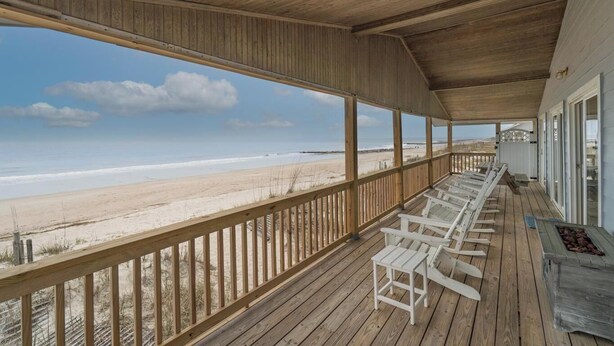 A covered deck with wooden railings overlooking a beach.