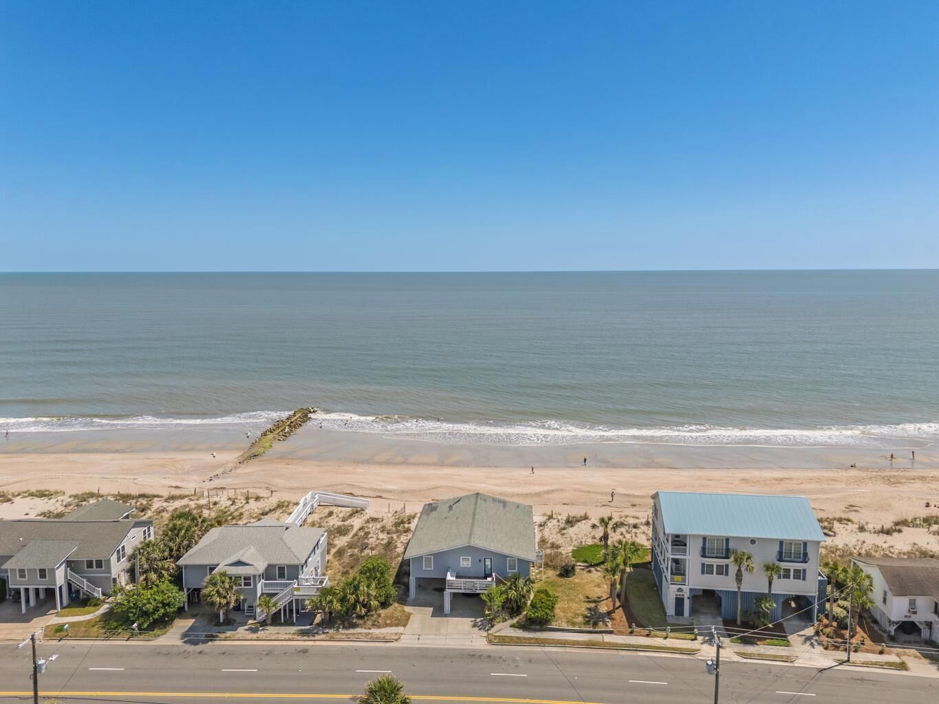 A coastal residential area with houses near the beach, a clear sky, and calm sea.