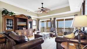 A spacious living room with leather sofas, a wooden entertainment center, and a large window overlooking a balcony.