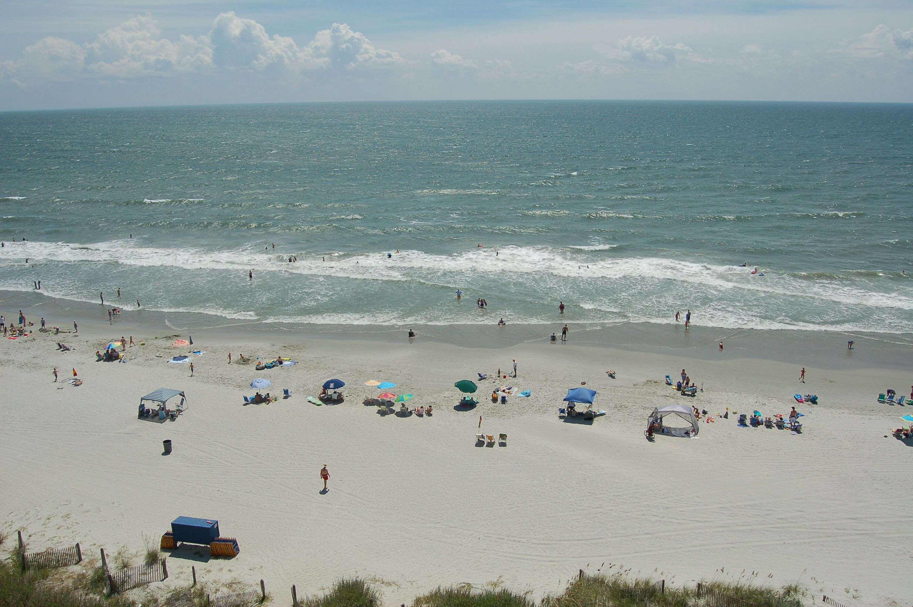 A beach with people, umbrellas, and beach chairs.