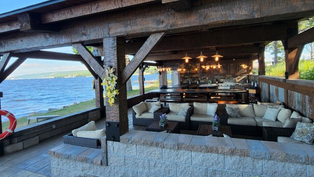 A covered outdoor seating area with stone walls, wooden beams, and a view of the water. - Kemp's Rentals Luxurious Executive Retreat Portage Lake-Beach-Firepit & Pavilion (Hancock)