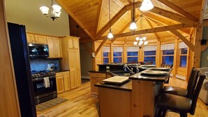 A spacious kitchen with wooden cabinets, a central island, and a dining area with bar stools. - Kemp's Rentals Luxurious Executive Retreat Portage Lake-Beach-Firepit & Pavilion (Hancock)