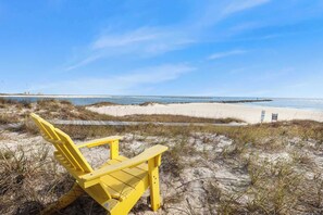 Une chaise de plage posée sur une dune de sable, avec vue sur l’océan et une jetée au loin.