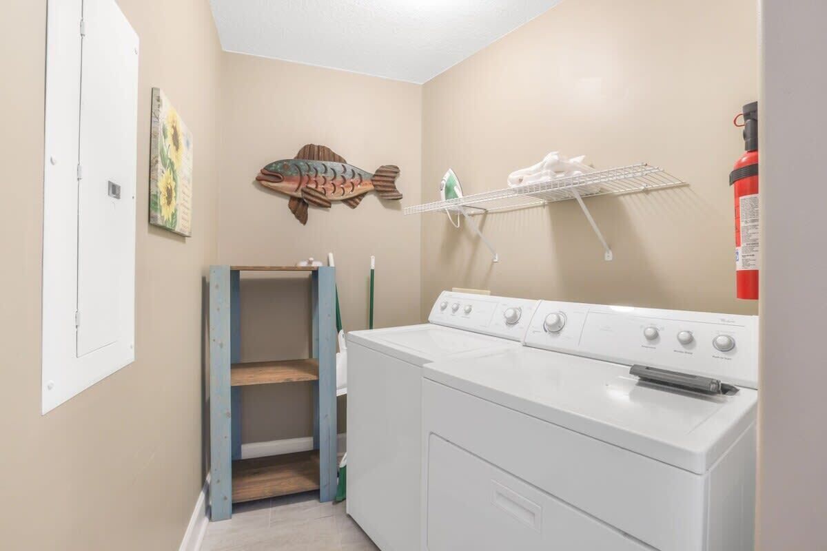 A laundry room with a washer and dryer, a shelf with cleaning supplies, a fish decoration, and a fire extinguisher.