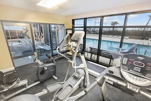 A gym with treadmills, elliptical machines, and a rowing machine, overlooking a pool.