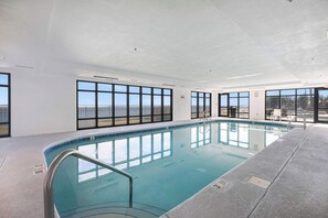 An indoor swimming pool with clear views through large windows, a tiled floor, and a metal pool ladder. - Grand Pointe 502- Gulf-front, water on 2 sides (Orange Beach)