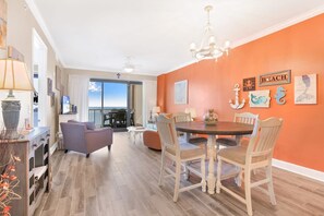 Un coin repas avec une table ronde et des chaises, un lustre et une vue sur l’océan par une porte coulissante.