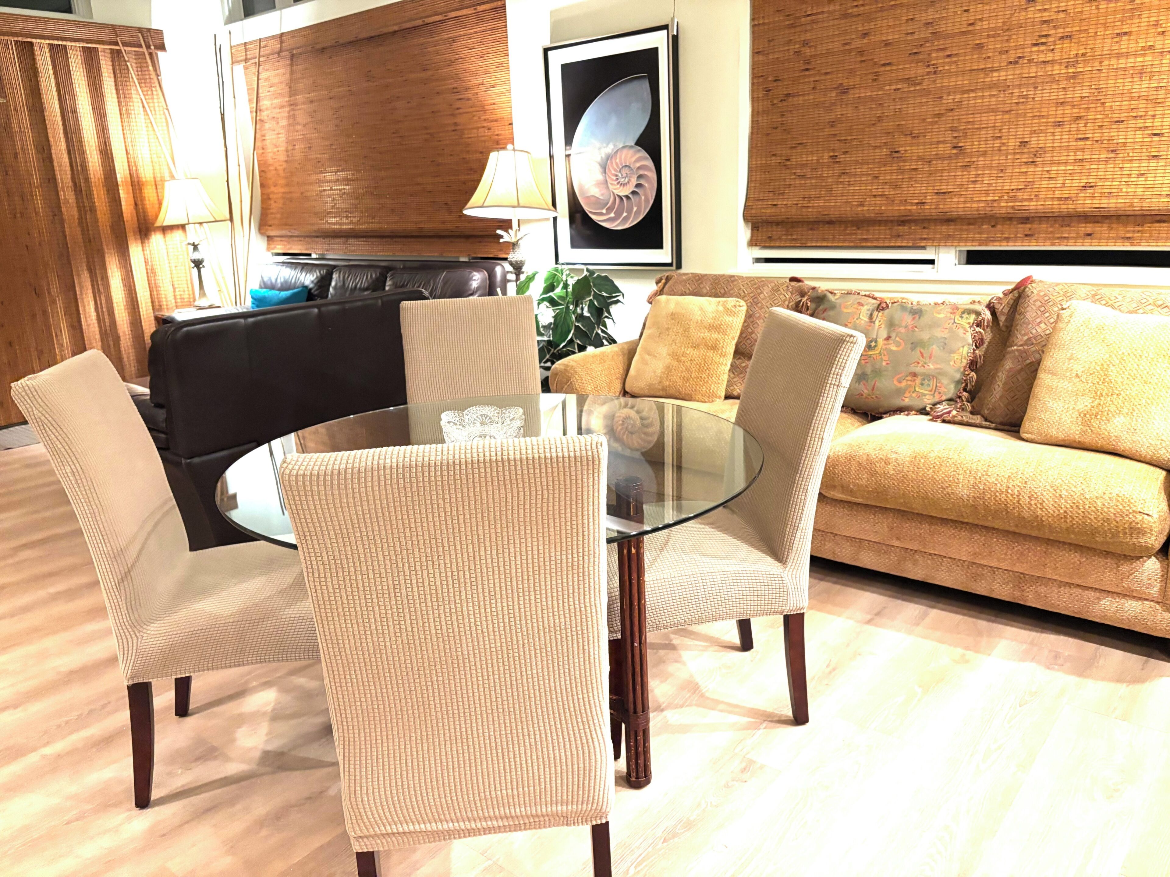 A living room with a glass-top coffee table, two chairs, a sofa, and a framed artwork on the wall.