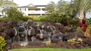 A landscaped garden with a cascading waterfall, surrounded by rocks and various plants. - AWESOME OCEANVIEW 3 BEDROOM 3 BATH TOWNHOME UNBEATABLE LOCATION (Kailua-Kona)