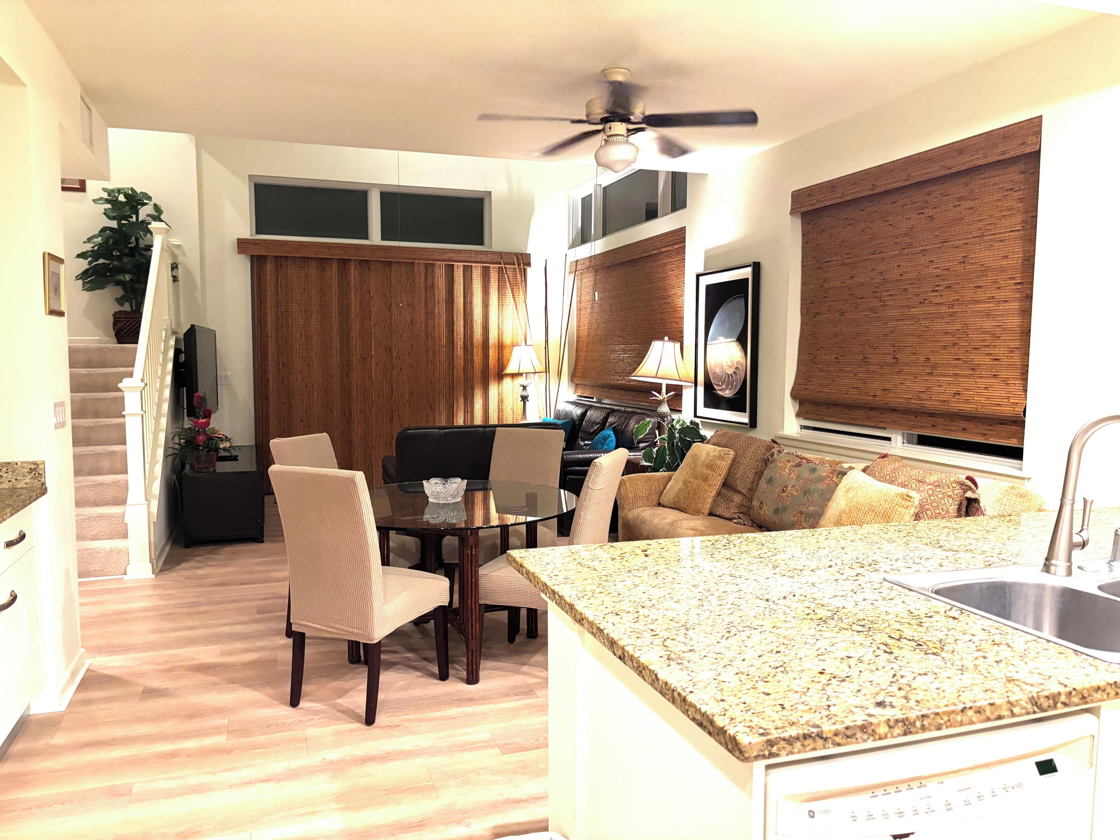 Una cocina moderna con encimera de granito, un comedor con mesa de vidrio y una sala de estar con sofá y televisor.
