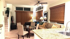 A modern kitchen with a granite countertop, a dining area with a glass table, and a living space with a sofa and a TV. - AWESOME OCEANVIEW 3 BEDROOM 3 BATH TOWNHOME UNBEATABLE LOCATION (Kailua-Kona)