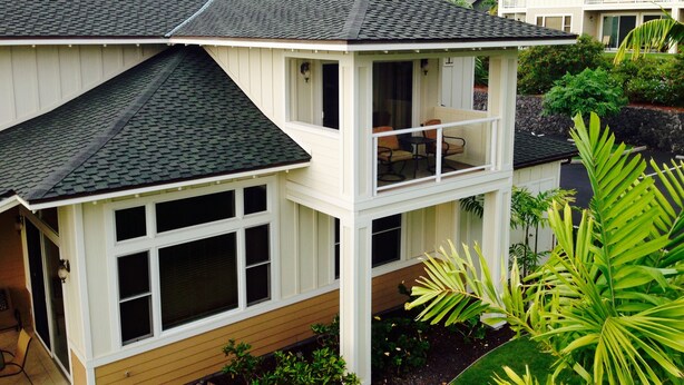 A two-story house with a balcony, large windows, and a view of a hilly landscape. - AWESOME OCEANVIEW 3 BEDROOM 3 BATH TOWNHOME UNBEATABLE LOCATION (Kailua-Kona)