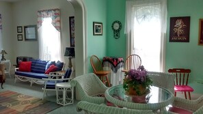 Un salon chaleureux avec un canapé bleu, des fauteuils en osier blancs, une table basse en verre agrémentée d’un arrangement floral, et une table à manger avec des chaises.