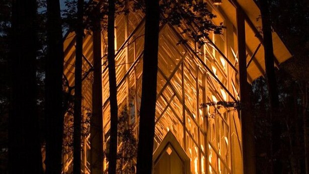 Een modern gebouw met een puntig dak en grote glasramen, omgeven door bomen.