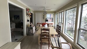 Een ruime eethoek met een grote houten tafel, verschillende stoelen en uitzicht door grote ramen.