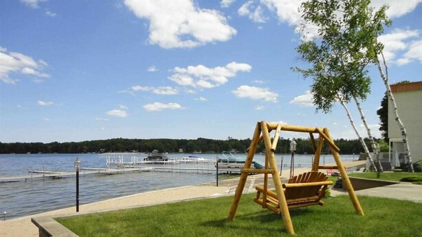 Une balançoire installée près d’un lac, avec un quai et des bateaux en arrière-plan.