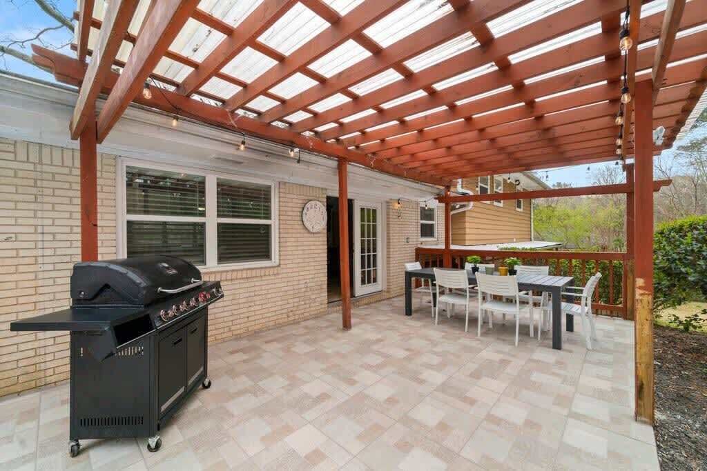 An outdoor patio with a grill, a table with chairs, and a pergola structure.