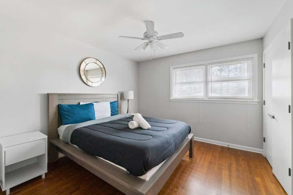 Un dormitorio con cama, mesita de noche, ventilador de techo, ventana con persianas y puerta.