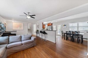 Un salón amplio con sofá, mesa de comedor con sillas, zona de cocina y ventilador de techo.
