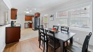 A modern kitchen with wooden cabinets, a dining table with chairs, and a large window with blinds. - Pool retreat near Atlanta, sleeps 14 (Decatur)