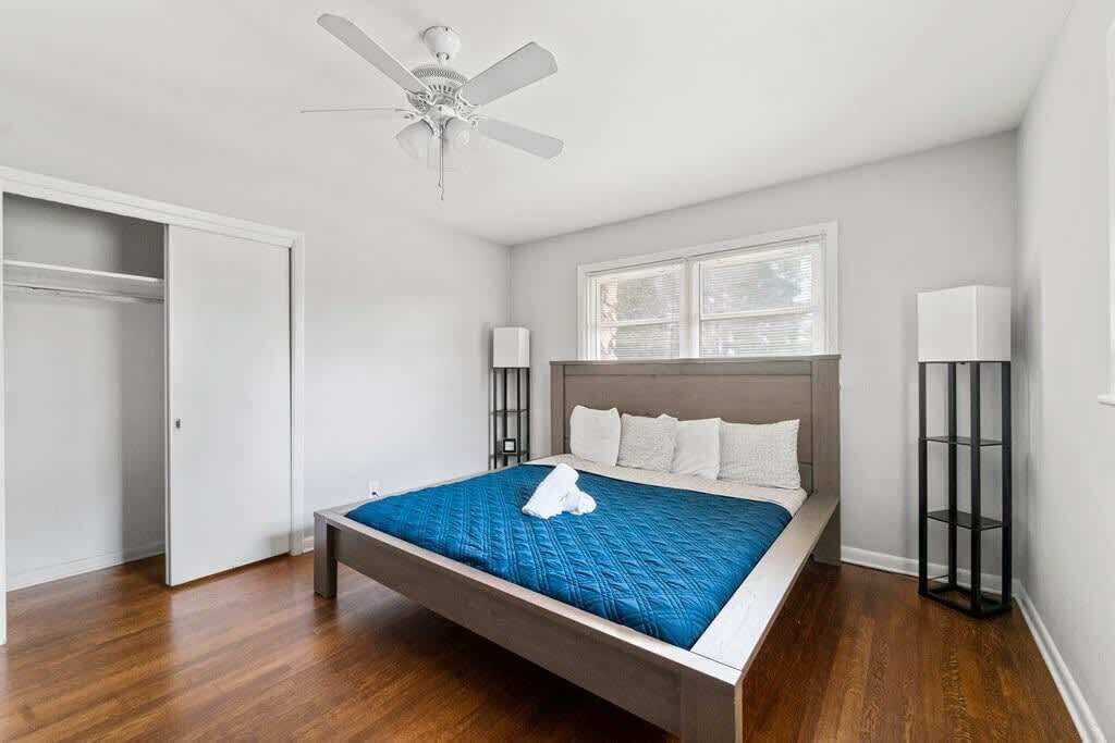 Un dormitorio con cama, ventilador de techo, ventana y mesita de noche.