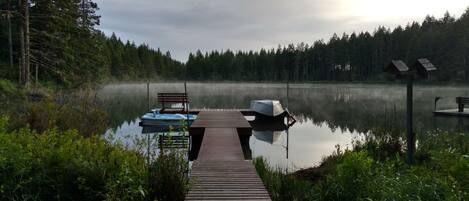 A wooden dock extending into a calm lake surrounded by dense forest.