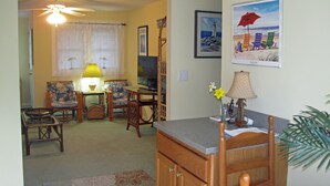 A living room with a television, two chairs, a dining table, and a kitchen area with cabinets and a countertop. - In-town Lewes location is near shops, museums, parks, bay and ocean beaches. (Lewes)