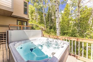 Ein Whirlpool auf einer Holzterrasse mit Blick auf Birken und ein Haus im Hintergrund.