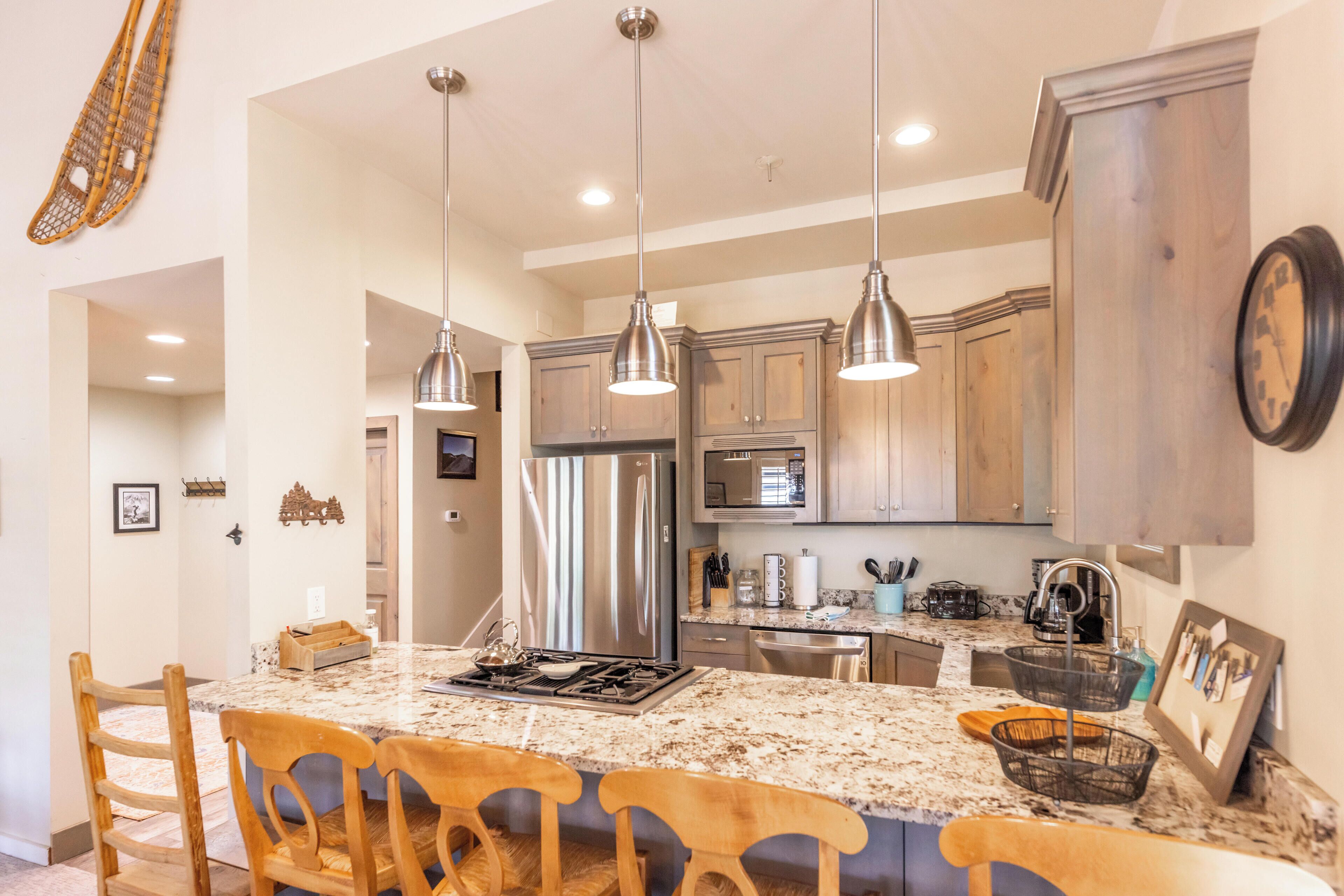 A kitchen with granite countertops, stainless steel appliances, wooden cabinets, and pendant lighting.
