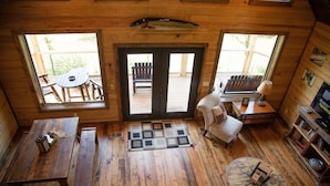 A wooden cabin interior with a dining table, a bench, a round table, a chair, and a bookshelf.